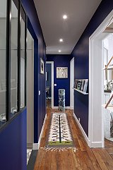Couloir d'entrée. Bleu de chine, tablettes sur support cuivre et cimaise à tableau. Aperçu de la verrière de la cuisine